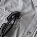 Close up of sunglasses hanging from front chest pocket of grey shirt