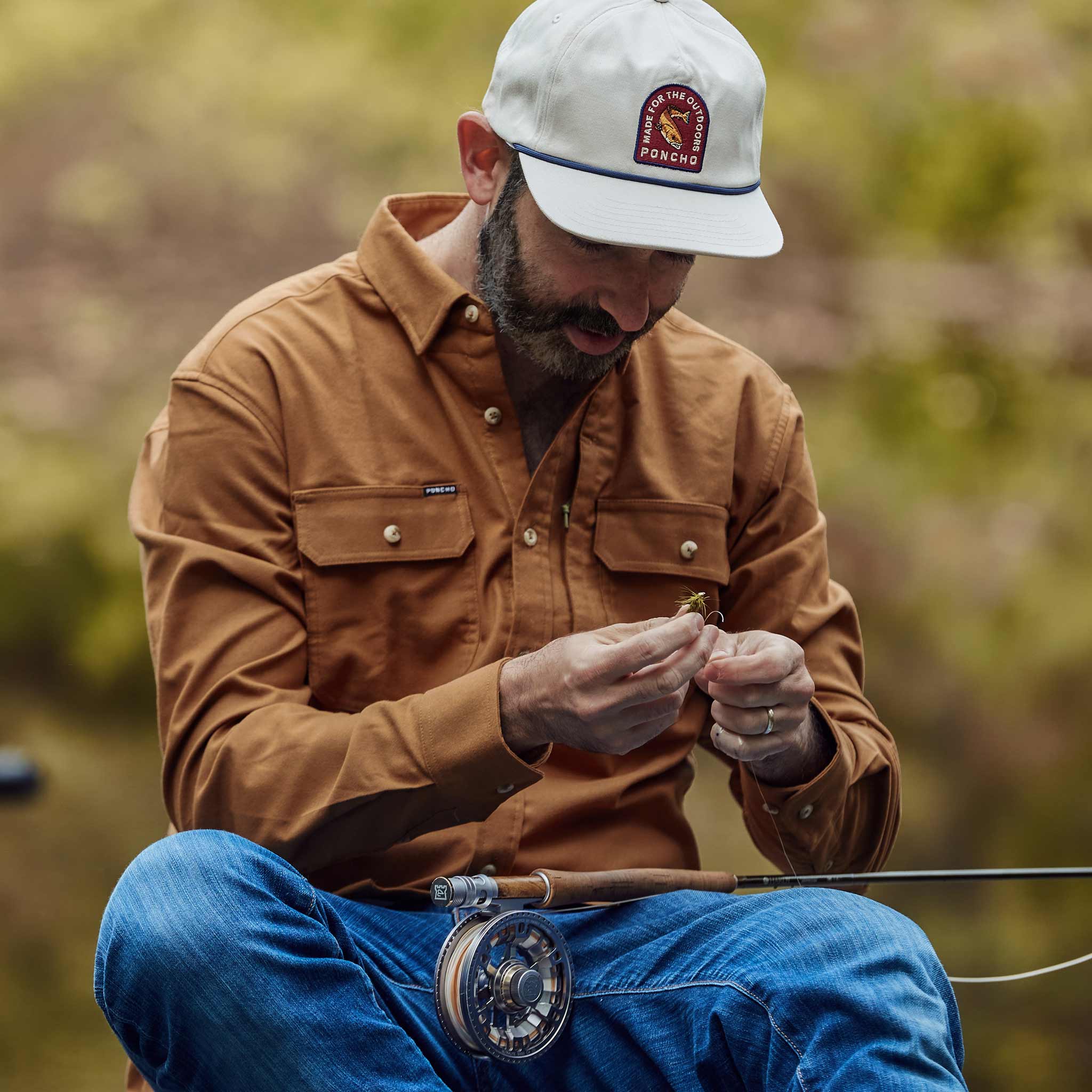 man with fishing rod in lap wearing light brown long sleeve flannel
