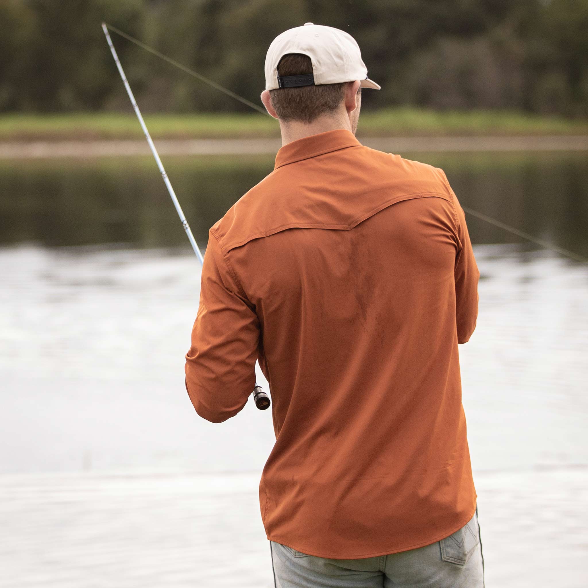 Man facing away from camera fishing while wearing burnt orange long sleeve shirt