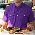 Man wearing short sleeve purple pearl snap shirt eating brisket and bbq