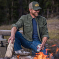 guy wearing olive green corduroy shirt sitting in front of campfire